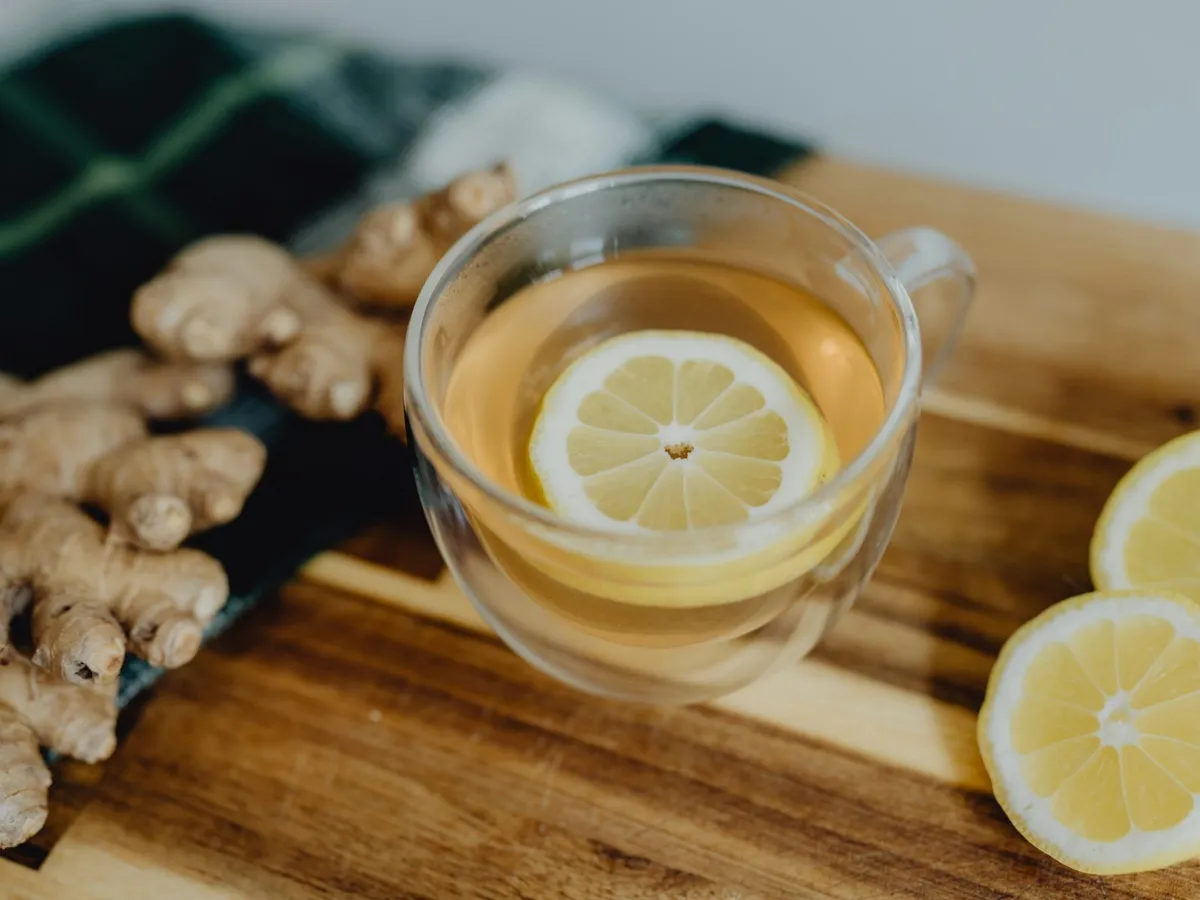 Ahşap tabla üzerinde taze zencefil, limon dilimleri ve bir bardak çay